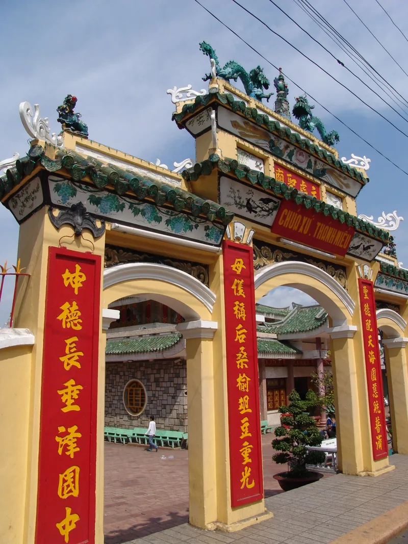Cổng chùa màu vàng với các câu đối chữ Hán đỏ và rồng trang trí trên nóc tại chùa Bà Chúa Xứ, Châu Đốc.