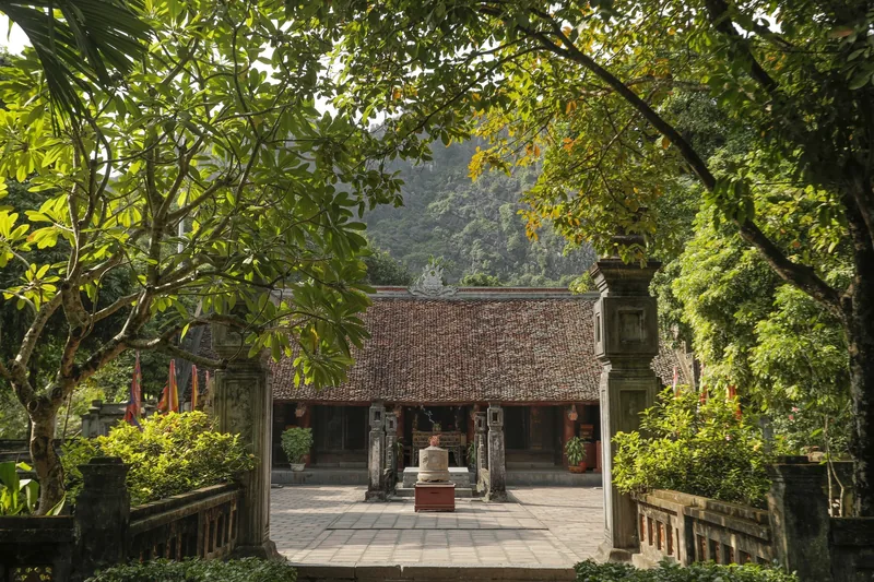 Sân đền mái ngói ở Hoa Lư, được bao quanh bởi cây xanh rậm rạp và núi đá vôi phía xa.