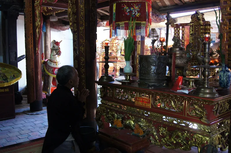 Một người lớn tuổi chắp tay khấn vái trước bàn thờ đỏ vàng lộng lẫy trong đền Trần, Nam Định.