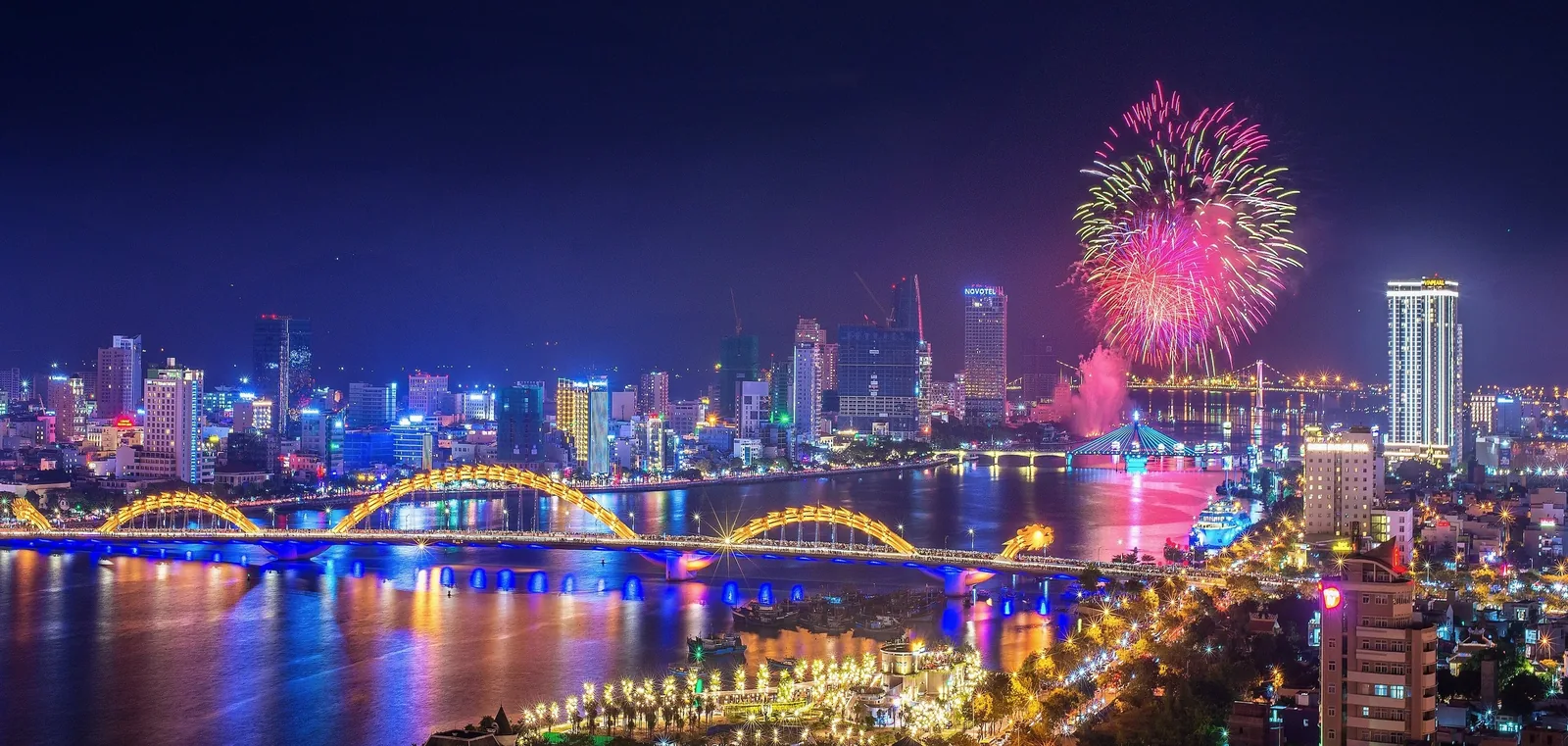 Pháo hoa rực sáng trên bầu trời đêm bên cầu Rồng và đường chân trời rực rỡ ánh đèn của Đà Nẵng.