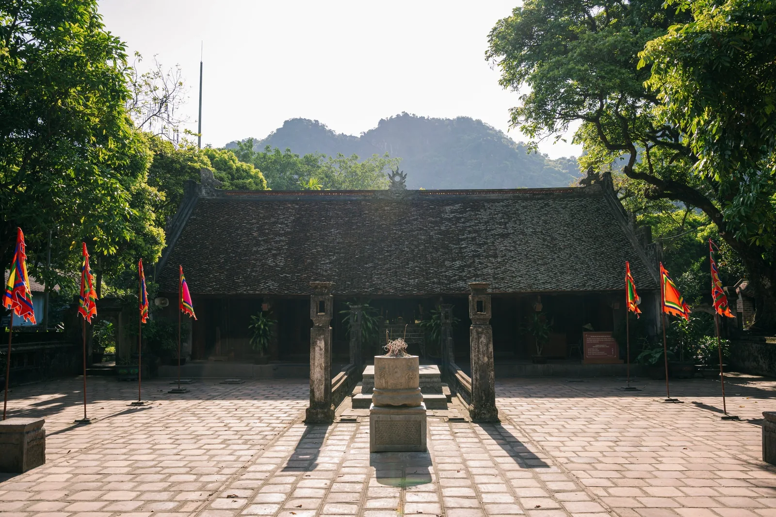Ngôi đền cổ với mái ngói rêu phong và cờ lễ hội sắc màu nổi bật trước núi đá vôi ở Hoa Lư, Ninh Bình.