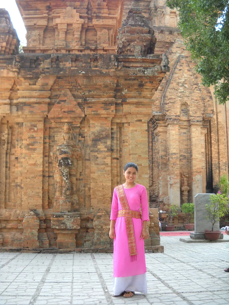 Một phụ nữ mặc áo dài hồng đứng trước những tháp gạch cổ Chăm ở Ninh Thuận.