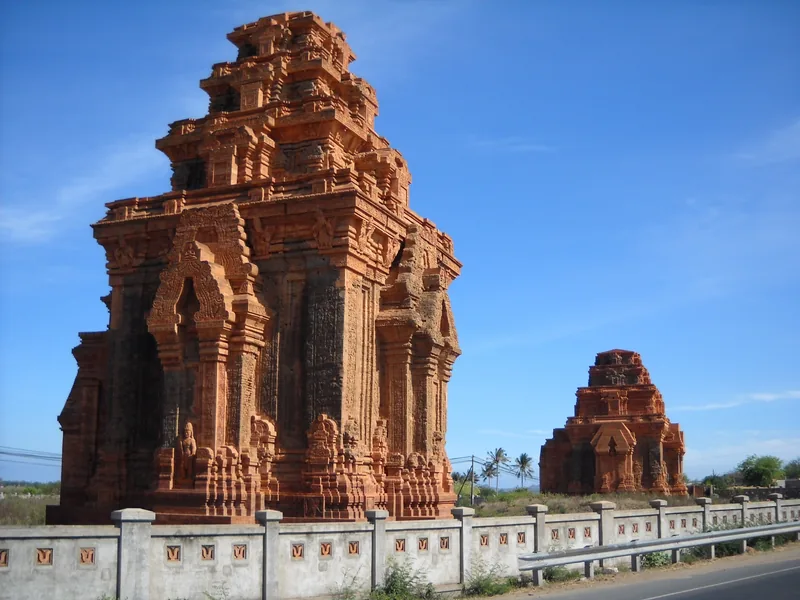 Các tháp Chăm gạch đỏ cổ của Hòa Lai đứng bên hàng rào ven đường dưới trời xanh ở Ninh Thuận.