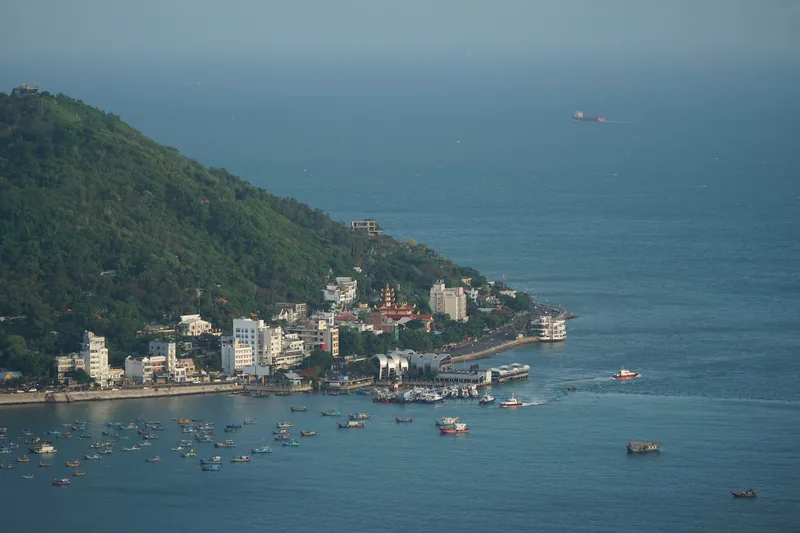 Ngọn núi xanh nhô ra biển bên cạnh thị trấn Vũng Tàu, với những chiếc thuyền cá rải rác trên vịnh.