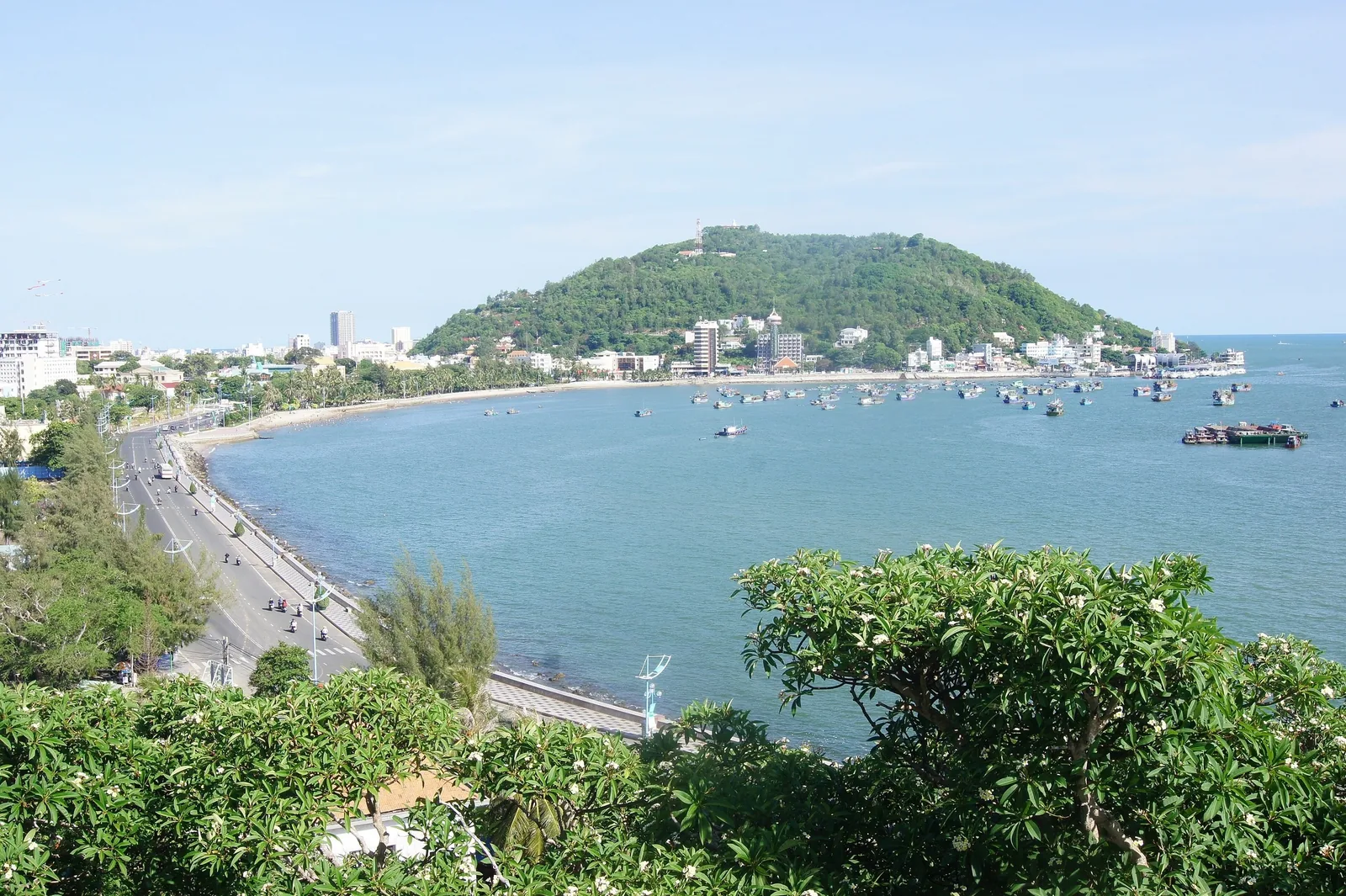 Con đường ven biển uốn cong dọc bãi biển Vũng Tàu, với thuyền cá neo đậu dưới ngọn núi xanh.