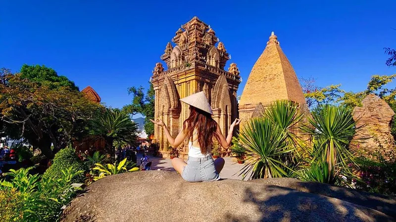 Một cô gái đội nón lá ngồi trên tảng đá hướng về tháp Po Nagar cổ kính ở Nha Trang.